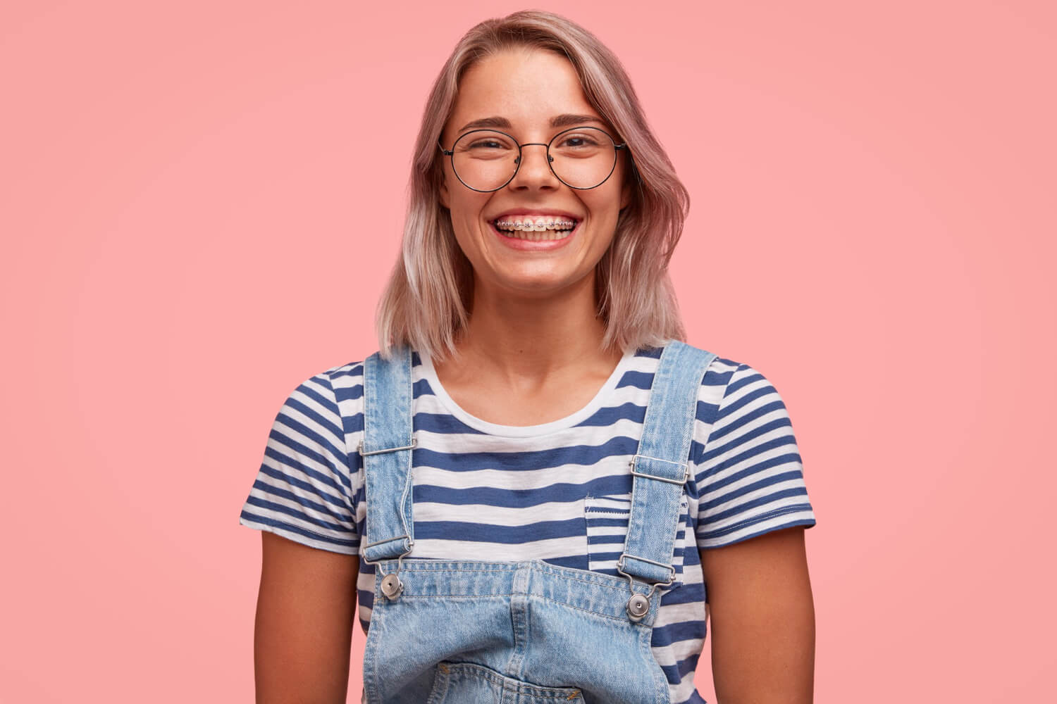 Mulher loira sorrindo com aparelho fixo e óculos, pronta para trocar aparelho por alinhadores invisíveis na Só Riso Odontologia.