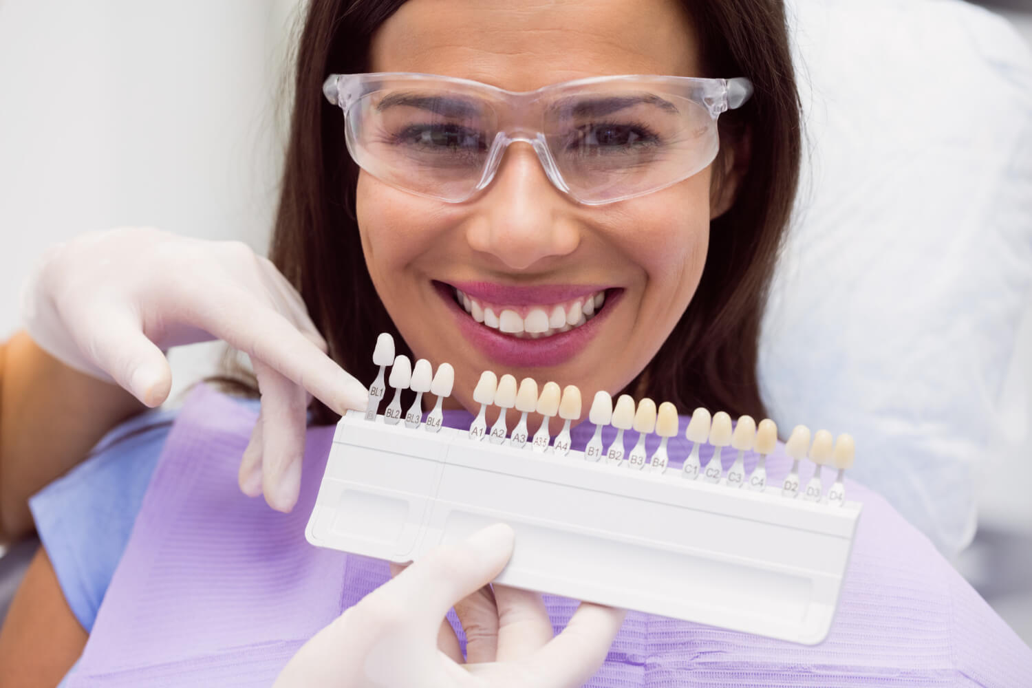 Mulher sorridente no dentista com escala de cores para lentes de contato dental em Patos de Minas. Foco em estética e durabilidade.