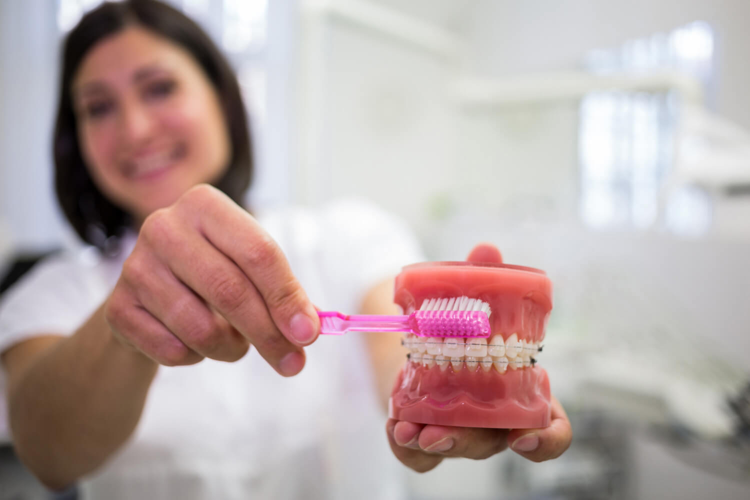 Dentista demonstra técnica de escovação com modelo dentário e escova rosa na So Riso para limpeza de prótese protocolo em Patos de Minas.