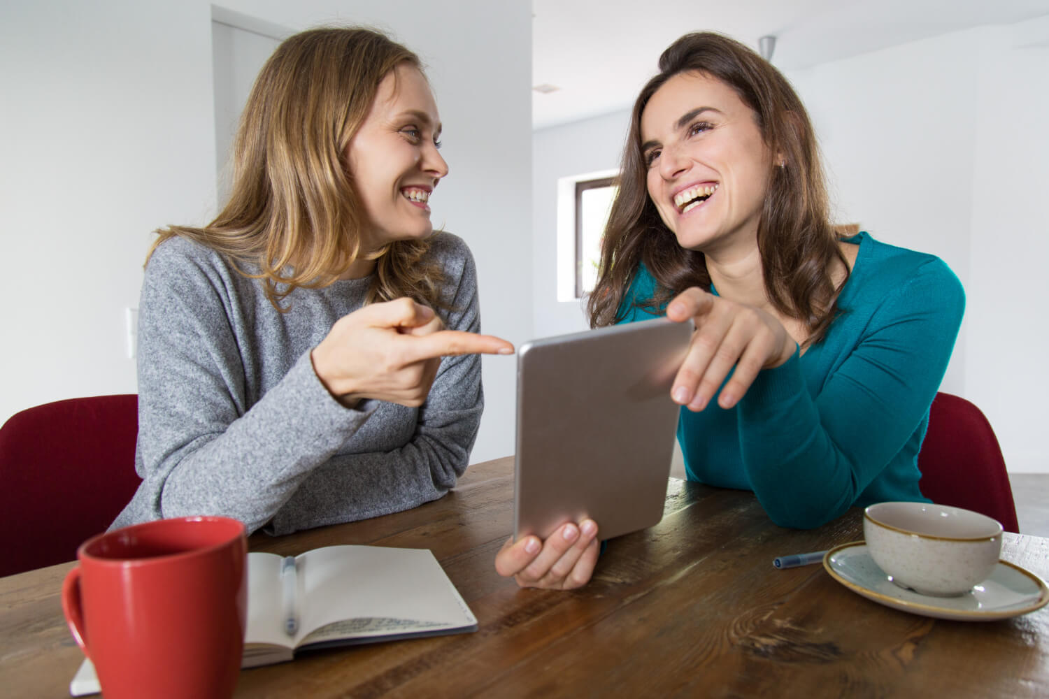 Duas mulheres sorridentes olhando um tablet. Entenda as fases do tratamento com implante dentário em Patos de Minas na Só Riso.